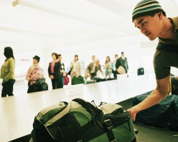 Travellers standing by airport carousel, young man picking luggage